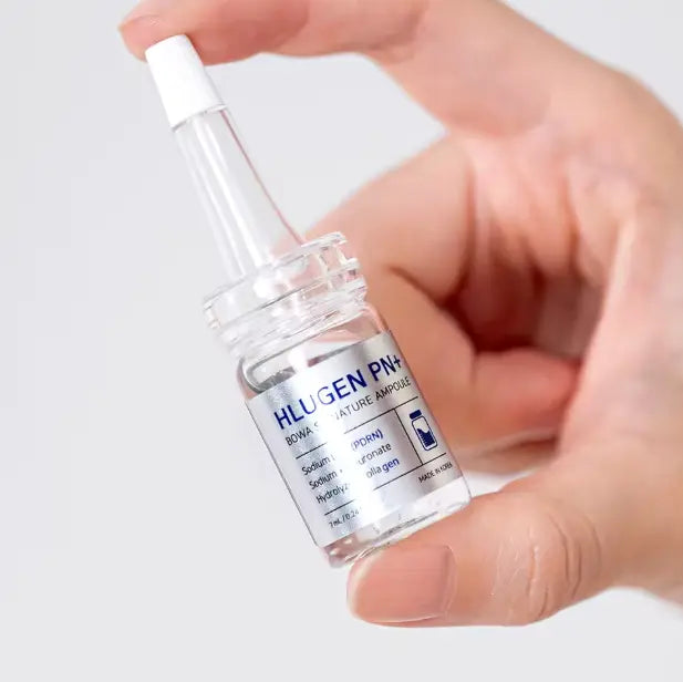 Hand holding a clear glass bottle labeled 'HLUGEN PN+' against a light background